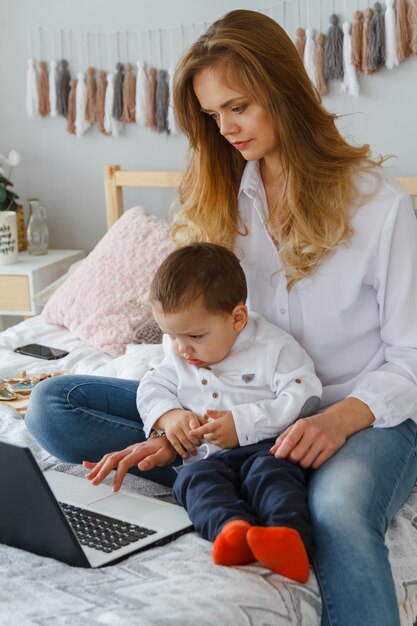 Eine junge Mutter mit ihrem geliebten Sohn im Schlafzimmer auf dem Bett mit einem Laptop