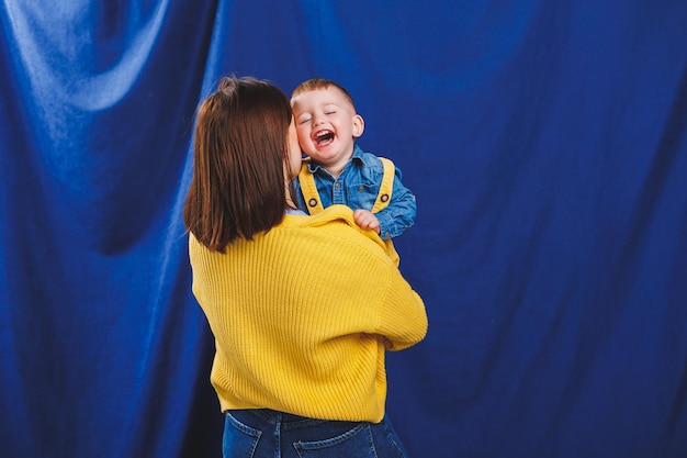 Eine junge Mutter spielt mit ihrem Kind auf blauem Hintergrund Familiäre Beziehung zum Kind Erziehung eines Kindes, das mit einem Kind spielt