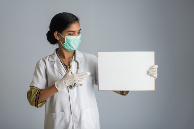 Eine junge Ärztin in einer medizinischen Maske, die eine leere Tafel hält, das Konzept einer Epidemie von Coronavirus, Covid-19.