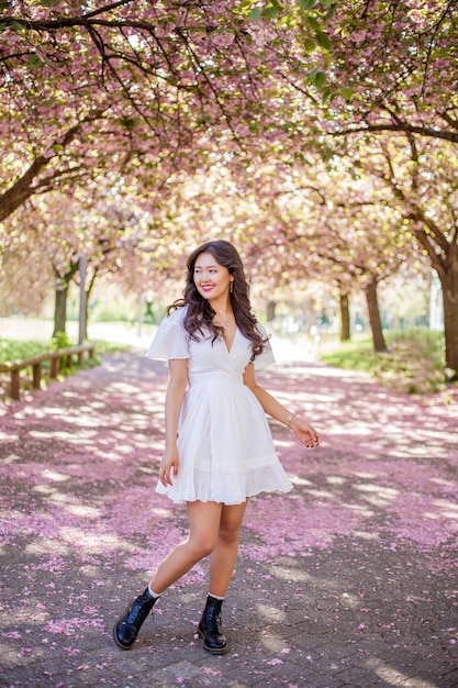 Eine junge schöne asiatische Frau in einem weißen Kleid geht in einem Blumenpark. Sakura. Blühende Bäume. Frühling.