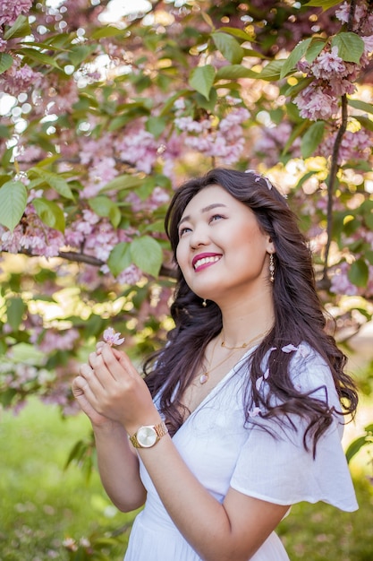Eine junge schöne asiatische Frau in einem weißen Kleid geht in einem Blumenpark