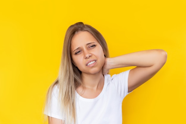 Eine junge schöne blonde Frau mit Nackenschmerzen, die ihren Hals auf gelbem Hintergrund hält