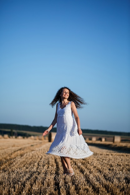 Eine junge schöne Frau in einem weißen Sommerkleid steht auf einem gemähten Weizenfeld mit riesigen Heugarben und genießt die Natur. Natur im Dorf. Selektiver Fokus