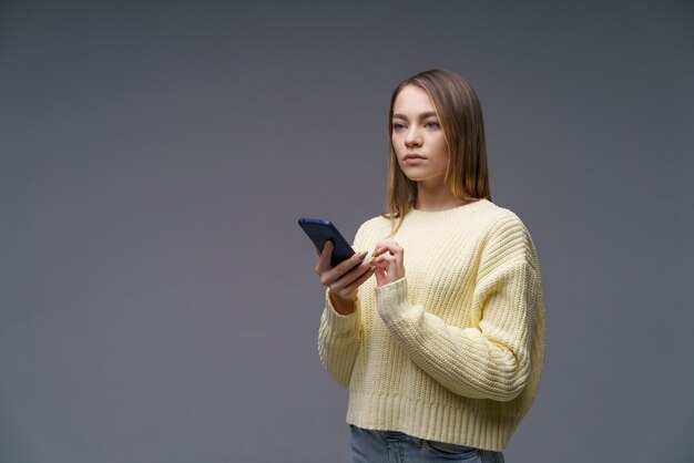 Eine junge schöne Frau kaukasischer Abstammung schreibt SMS am Telefon steht in einem gelben Pullover auf...