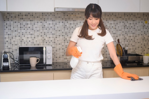Eine junge schöne Frau mit Gummischutzhandschuhen putzt den Tisch in der Küche zu Hause.