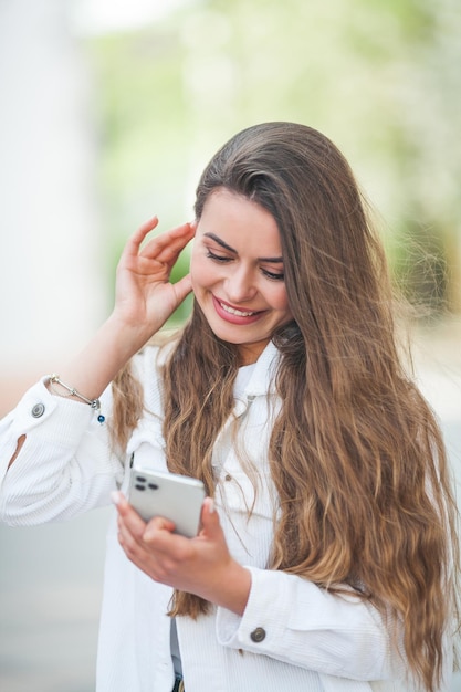 Eine junge schöne Frau mit langen Haaren in bequemer, leichter Freizeitkleidung hört Musik mit Bluetooth-Kopfhörern Spaziergänge im Zentrum einer europäischen Stadt Ein süßes Model kauft Frühling ein