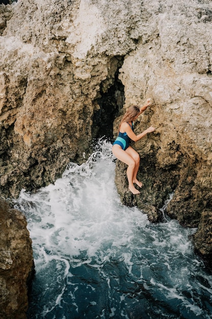 Eine junge schöne gebräunte Frau mit langen Haaren im blauen Bikini sitzt auf Felsen in der Nähe von blaugrün klar