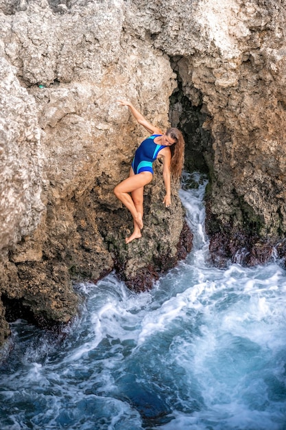 Eine junge schöne gebräunte Frau mit langen Haaren im blauen Bikini sitzt auf Felsen in der Nähe von blaugrün klar