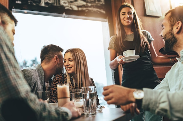 Eine junge schöne Kellnerin bedient eine Gruppe junger lächelnder Freunde in einem Café.