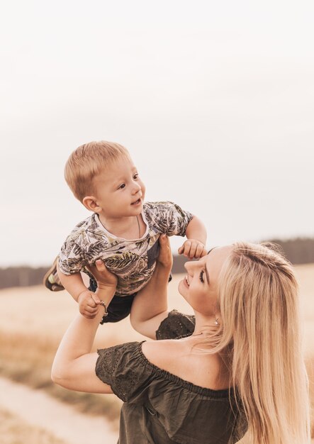 Eine junge schöne Mutter hält ihren kleinen Sohn in den Armen und spielt mit ihm im Sommer in der Natur.