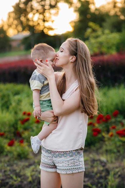 Eine junge schöne Mutter küsst und umarmt ihren kleinen Sohn während des Sonnenuntergangs im Park. Glücklicher Familienspaziergang im Park.