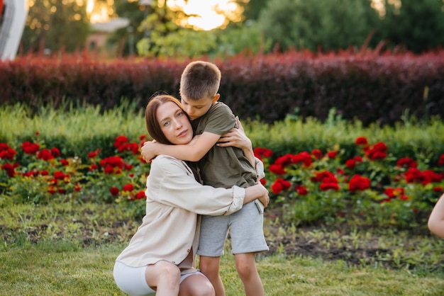 Eine junge schöne mutter küsst und umarmt ihren kleinen sohn während des sonnenuntergangs im park. glücklicher familienspaziergang im park.