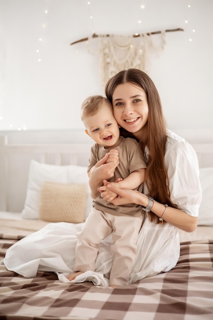 Eine junge schöne Mutter mit einem kleinen Jungen, der sich zu Hause im Schlafzimmer der Mutter auf dem Bett umarmt und Kinder und Eltern liebt
