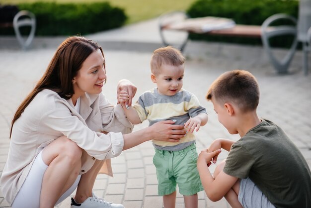 Eine junge schöne Mutter mit zwei kleinen Jungen spielt während des Sonnenuntergangs im Park. Glücklicher Familienspaziergang mit Kindern im Park.