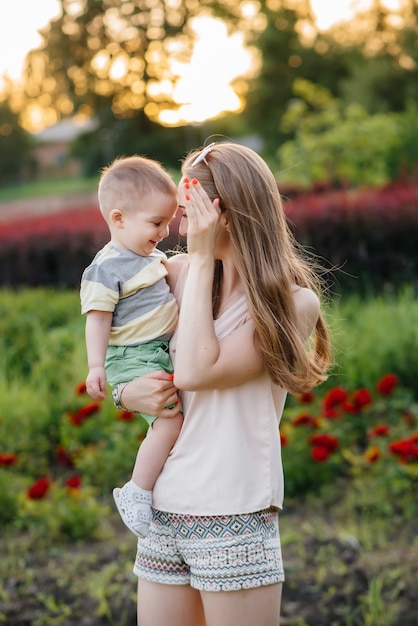 Eine junge schöne Mutter spielt und umarmt ihren kleinen Sohn während des Sonnenuntergangs im Park. Glücklicher Familienspaziergang im Park.