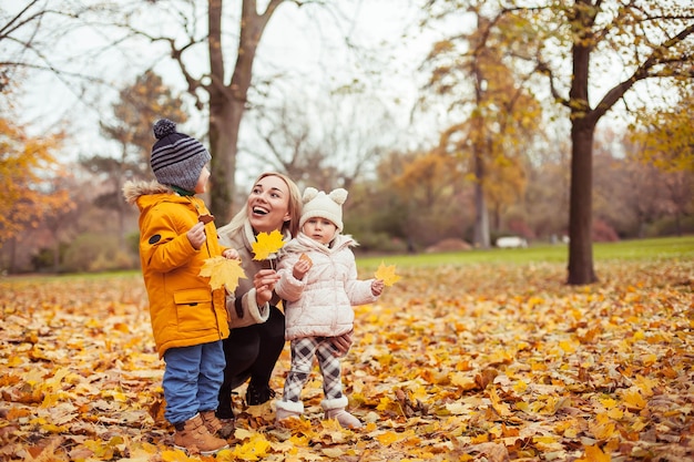 Eine junge schöne Mutter und zwei kleine Kinder gehen durch den Herbstpark. Mutter und zwei kleine Kinder spielen. Warmer Winter. Heller Herbst. Gemütlich.