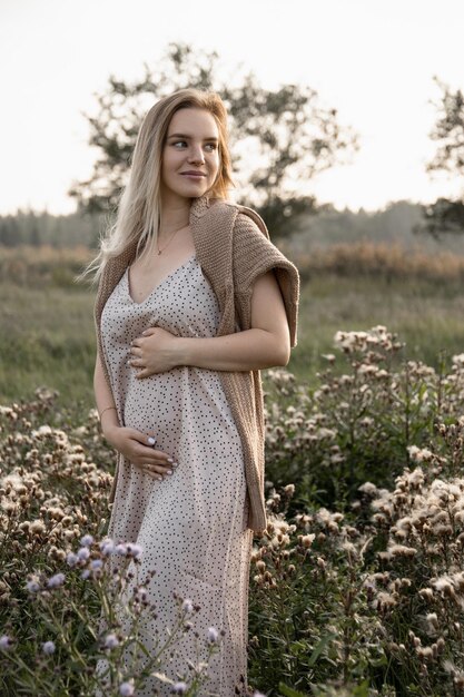 Eine junge schwangere Frau in einem Kleid umarmt ihren Bauch in Erwartung einer Geburt im Park Schwangerschaft