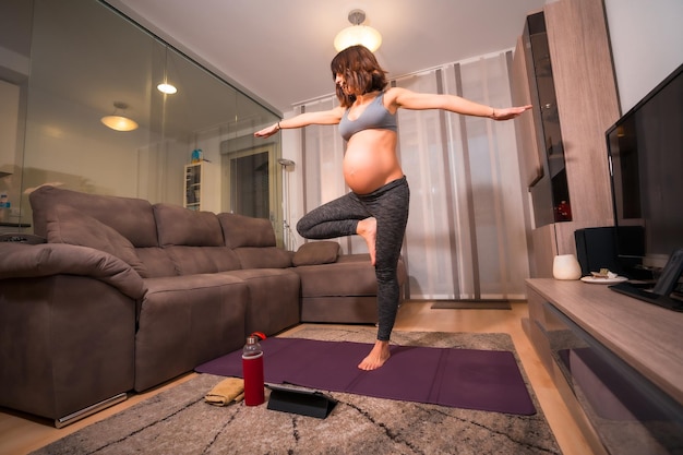 Eine junge schwangere kaukasische Frau, die zu Hause im Wohnzimmer Pilates-Übungen macht Online-Übungen in Prepartum-Kursen