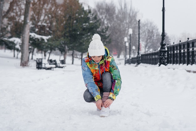 Eine junge sportliche Frau bindet ihre Schuhe an einem frostigen und schneereichen Tag. Fitness, Laufen