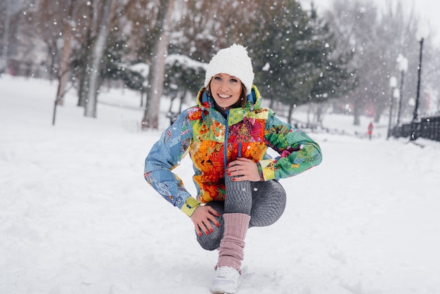 Eine junge sportliche Frau bindet ihre Schuhe an einem frostigen und schneereichen Tag. Fitness, Laufen