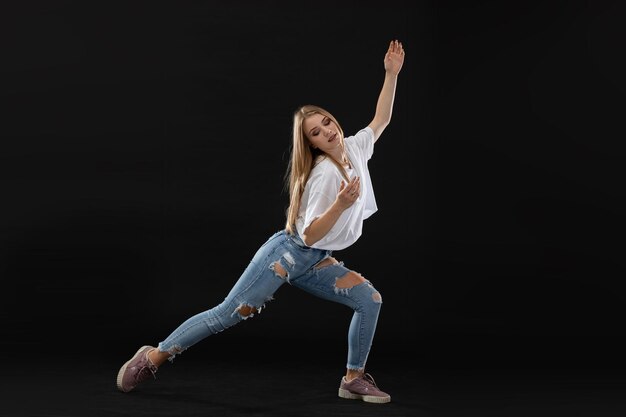 Eine junge Tänzerin führt eine Pose aus einer Tanzroutine aus, während sie weit auseinander steht und der Kamera gegenüber steht. Lange blonde Haare