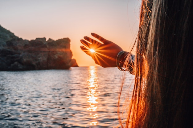 Eine junge Touristenfrau, die eine Kaffeetasse hält, während sie im Freien sitzt und den Sonnenaufgang über dem Meer genießt?