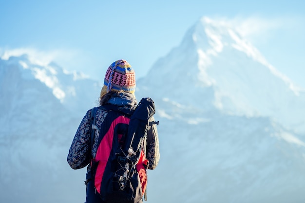 Eine junge Touristenfrau mit Wanderrucksack und Strickmütze im Himalaya-Gebirge. Trekking-Konzept in den Bergen.