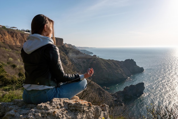 Eine junge Touristin, die den Sonnenuntergang über der Berglandschaft genießt, während sie im Freien sitzt Yoga-Fitness-Routine für Frauen Gesunder Lebensstil, Harmonie und Meditation