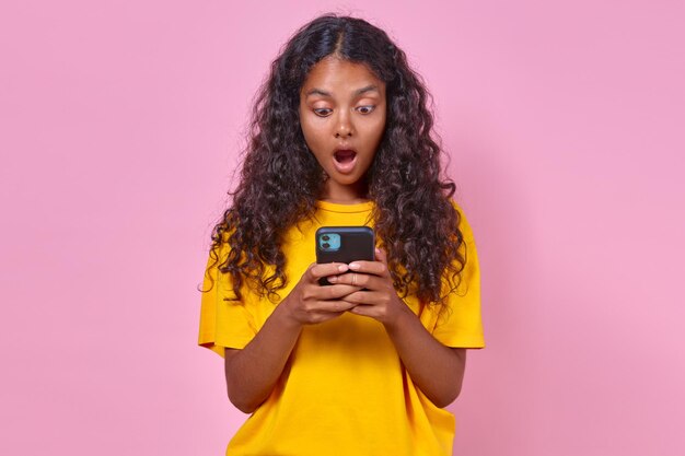 Eine junge überraschte indische Frau, eine Teenagerin, die ein Telefon in der Hand hält, steht im Studio.