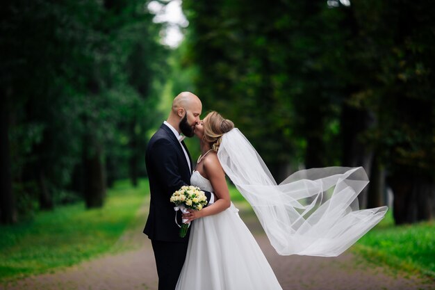 Eine junge und schöne Braut und ihr Ehemann stehen in einem Sommerpark mit Blumenstrauß