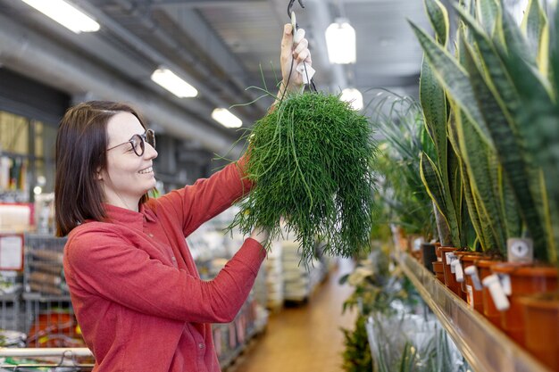 Eine junge und schöne kaukasische Frau in einem rosa Hemd wählt Blumen in einem Blumenladen aus