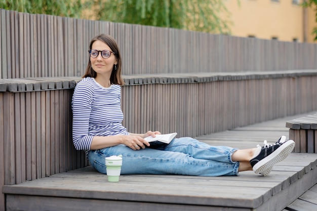 Eine junge und selbstbewusste europäische Frau ruht sich aus und liest ein Buch, eine Frau trinkt Kaffee entspannt oder