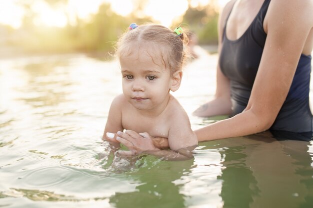 Eine junge unerkennbare Mutter, die ein kleines Baby hält, das lernt zu schwimmen.