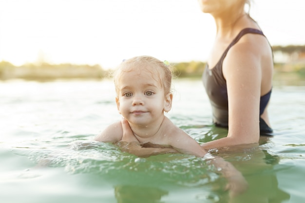 Eine junge unerkennbare Mutter, die ein kleines Baby hält, das lernt zu schwimmen.