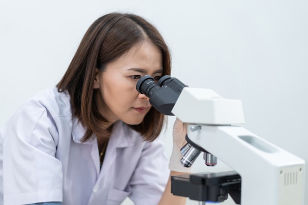 Eine junge Wissenschaftlerin in einem Laborkittel, die in einem Labor durch ein Mikroskop schaut, um zu forschen und zu experimentieren. Wissenschaftler, der in einem Labor arbeitet. Bildung stockfoto