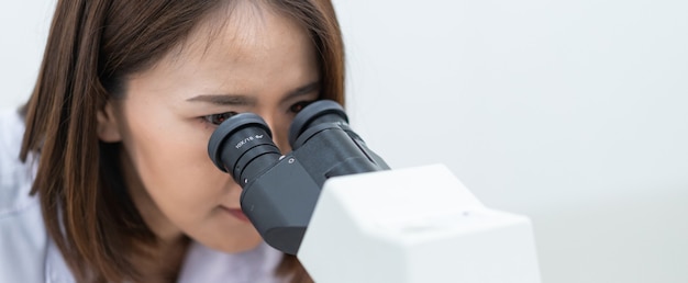 Eine junge Wissenschaftlerin in einem Laborkittel, die in einem Labor durch ein Mikroskop schaut, um zu forschen und zu experimentieren. Wissenschaftler, der in einem Labor arbeitet. Bildung stockfoto