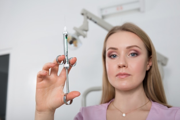 Eine junge Zahnarztfrau, die eine Spritze vor dem Hintergrund einer Zahnarztpraxis hält