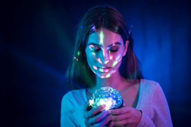 Eine kaukasische Frau des jungen Brunette in einem weißen T-Shirt auf einem schwarzen Hintergrund. Neonlichter, beleuchtet mit einem Discolicht in der Hand