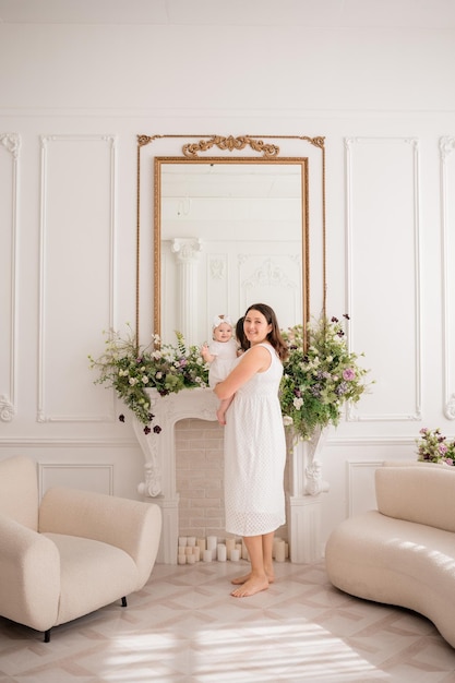 Eine kaukasische mutter in einem weißen kleid steht mit ihrer kleinen tochter in einem raum mit einem schönen interieur