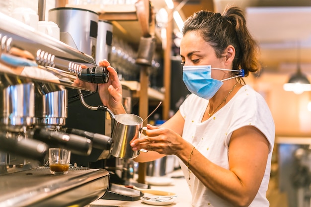 Eine Kellnerin mit einer Gesichtsmaske in einer Bar. Kaffee zubereiten