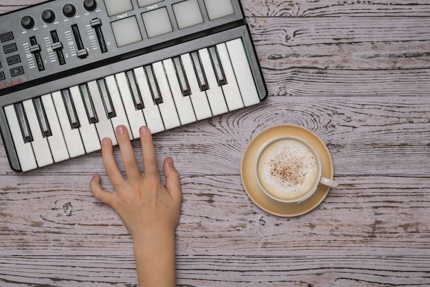 Eine Kinderhand auf den Tasten eines Musikmischers und eine Tasse Kaffee auf einem Holztisch. Der Prozess des Musikschaffens