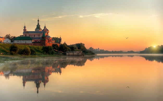 eine Kirche am Ufer eines Flusses mit einem Sonnenuntergang im Hintergrund