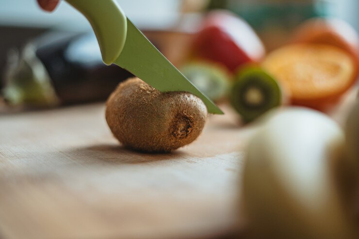 Foto eine kiwis, die auf einem holztisch, umgeben von anderen früchten, geschnitten wird.