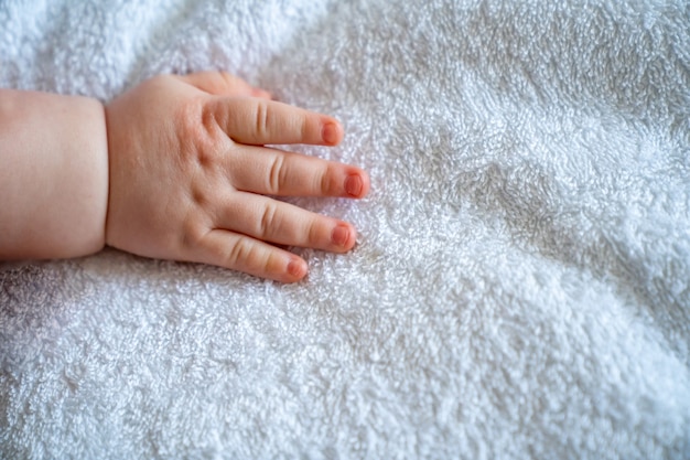 Eine kleine Babyhand auf weißem Laken