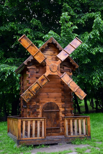 Eine kleine dekorative braune Holzmühle steht im Garten vor dem Hintergrund von Bäumen auf einem Steinsockel