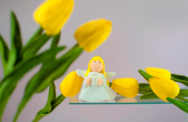 Eine kleine Figur eines Engels mit einem Strauß gelber Tulpen auf einem rosa Hintergrund. ein sanftes Bild der Feiertage am 8. März, Muttertag, Frühlingssaison. kopierraum, weicher fokus.