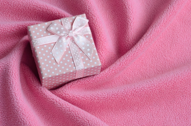 Eine kleine Geschenkbox in Rosa mit einer kleinen Schleife liegt auf einer Decke