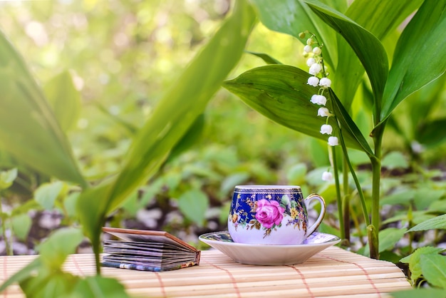 Eine kleine Tasse Tee neben den Blumen der Maiglöckchen