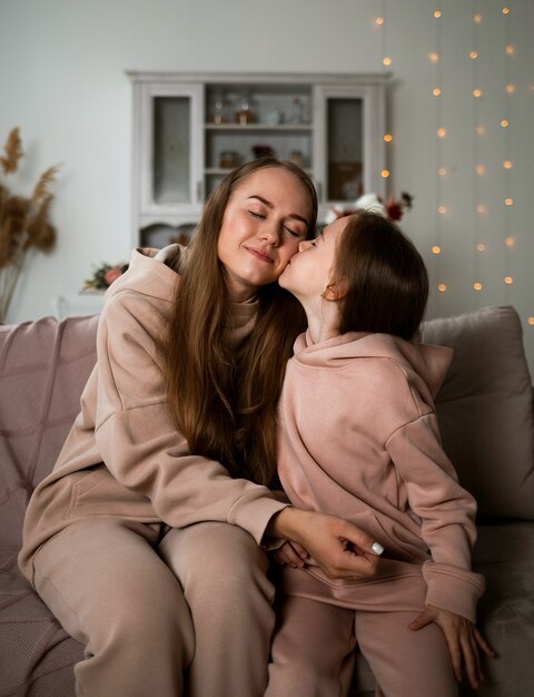 Eine kleine Tochter sitzt auf der Couch und küsst ihre Mutter