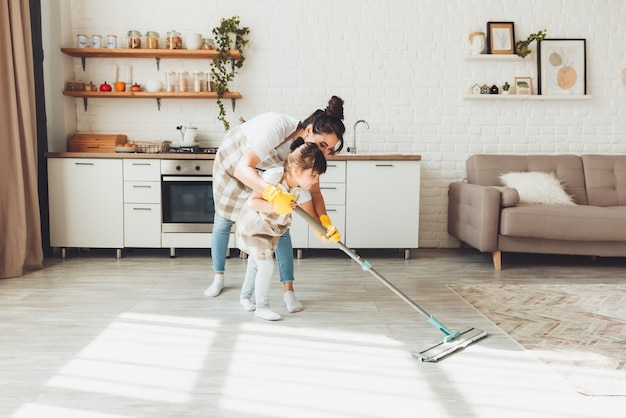 Eine kleine Tochter und ihre Mutter putzen das Haus, ein Kind wäscht den Küchenboden, ein süßes kleines Helfermädchen putzt den Boden mit einem Mopp, eine glückliche Familie putzt das Zimmer